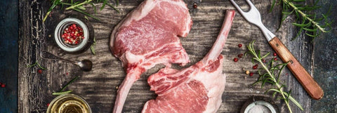 Beautifully fat marbled pork chops on a wooden slab with herbs and flaky salt