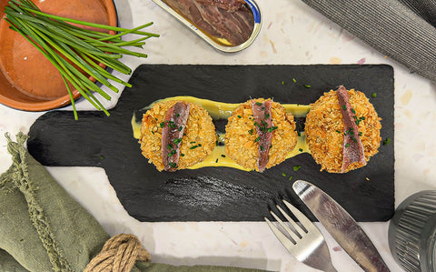 Black chalk board with three golden croquetas topped with anchovies and green chives 